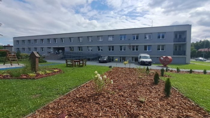 Budynek szkoły w otoczeniu krzewów i roślin ozdobnych.