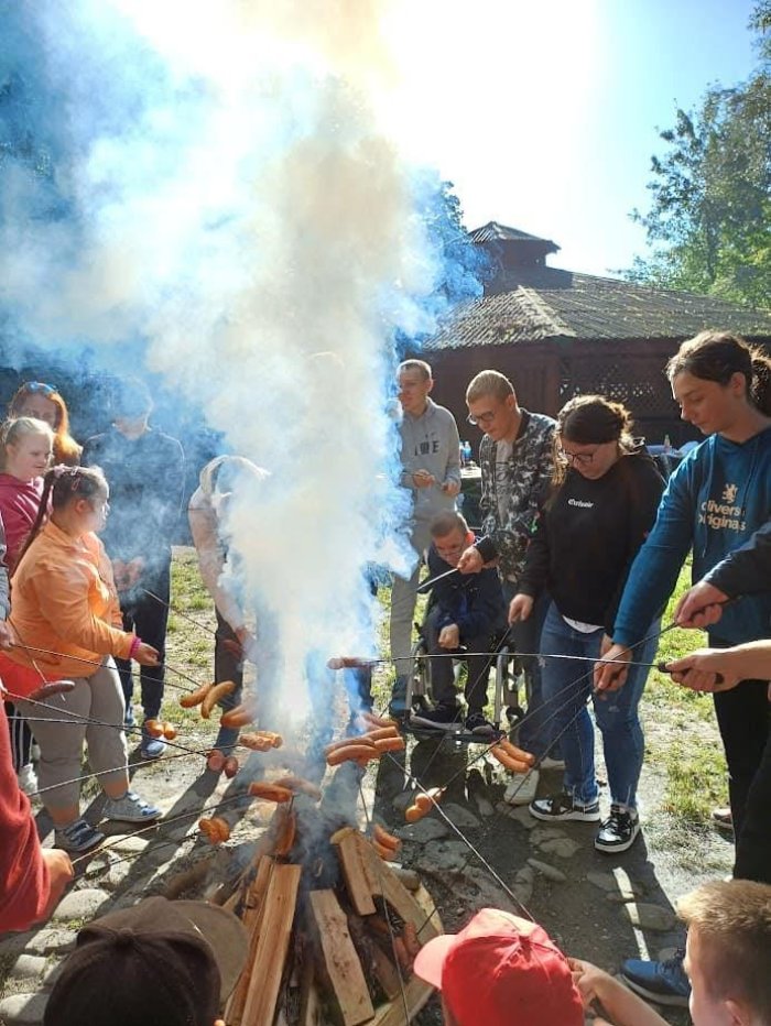 Uczniowie pieką kiełbaski przy ognisku.