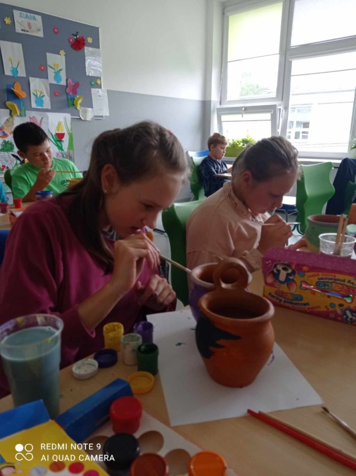 Uczniowie malują doniczki ceramiczne.