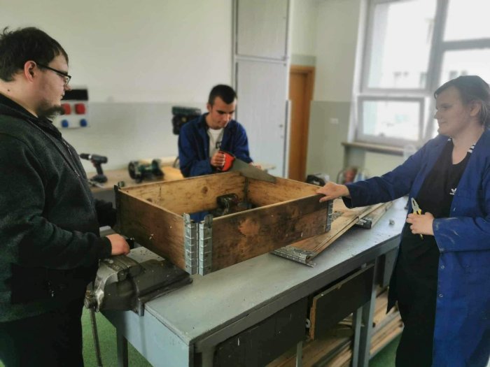 Uczniowie klasy przysposabiającej do pracy skręcają drewnianą skrzynkę w pracowni stolarskiej. 
