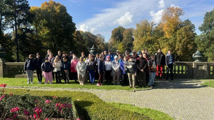 Uczniowie pozują do zdjęcia na tle ogrodów zabytkowego parku pszczyńskiego.