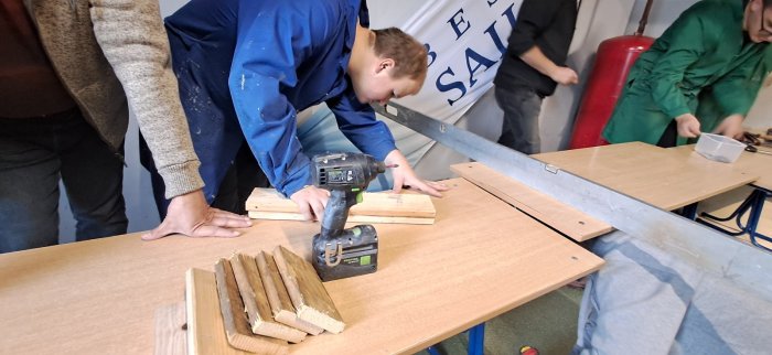 Uczeń pod opieką nauczycieli używa narzędzi stolarskich.