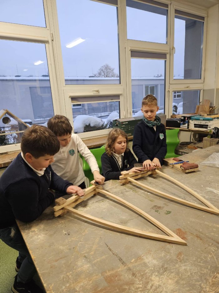 Uczniowie przygotowują z drewna elementy łódki.