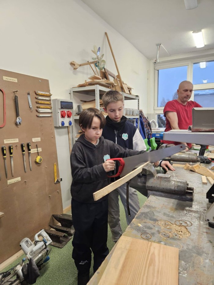 Uczniowie pod okiem nauczyciela szlifują elementy do łódki.