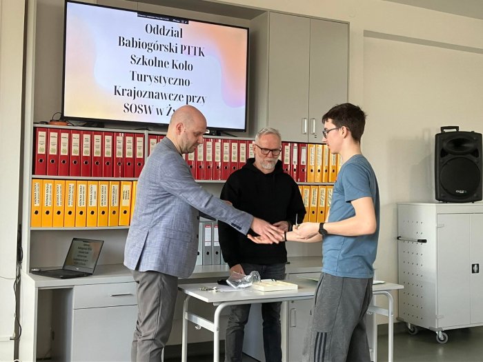 Sekretarz Oddziału Babiogórskiego PTTK wręcza uczniowi legitymację członkowską.