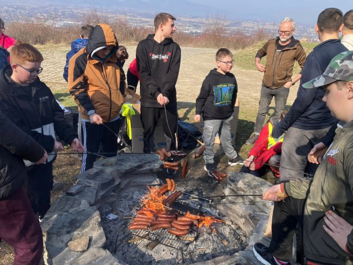 Uczniowie pieką kiełbaski na ognisku.