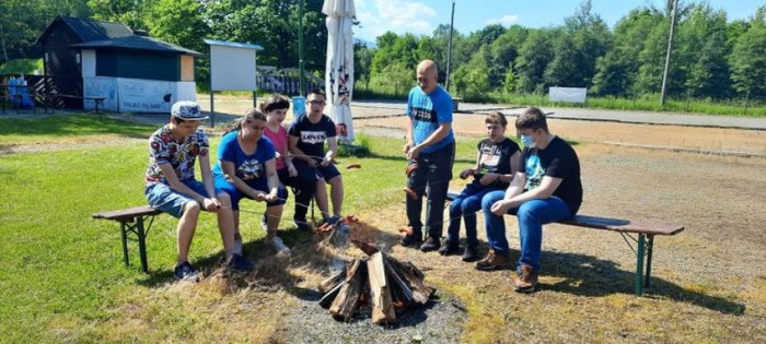 Uczniowie smażą kiełbaski na ognisku.