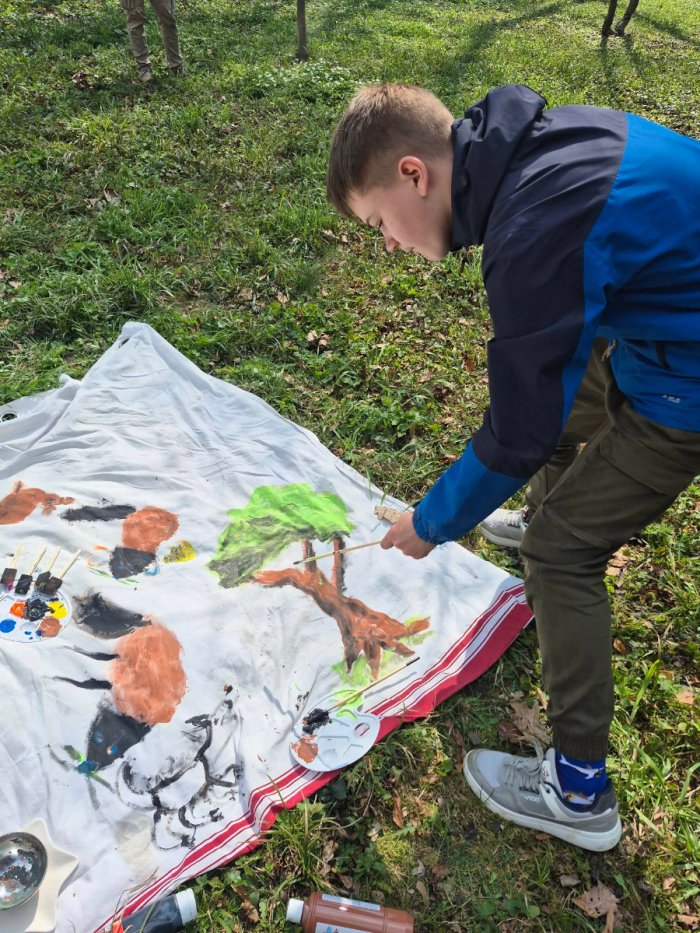 Uczeń maluje drzewo na płótnie farbami akrylowymi.