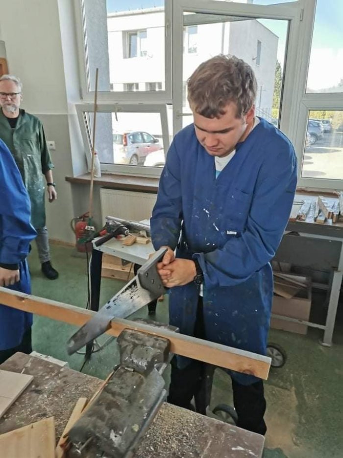 Uczeń przecina kawałek drewna. 