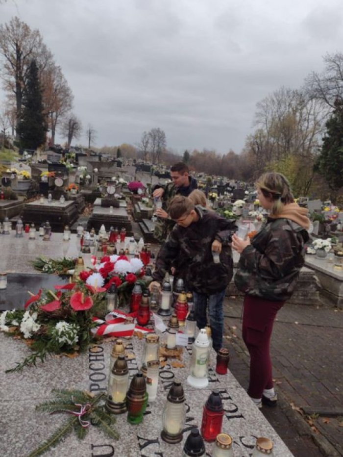 Harcerze zapalają znicze na grobach żołnierzy.