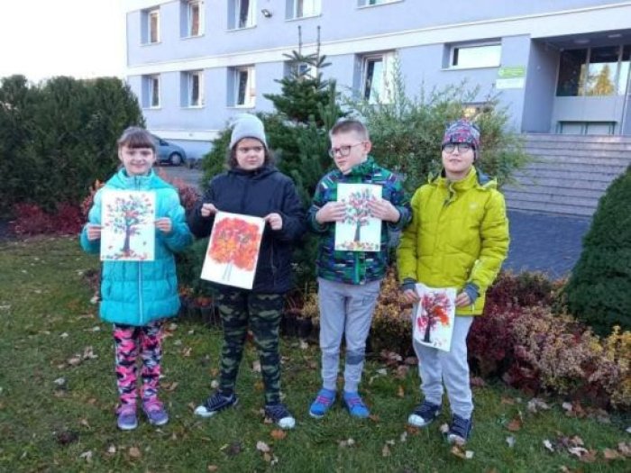 Uczniowie prezentują na tle szkoły swoje prace plastyczne.