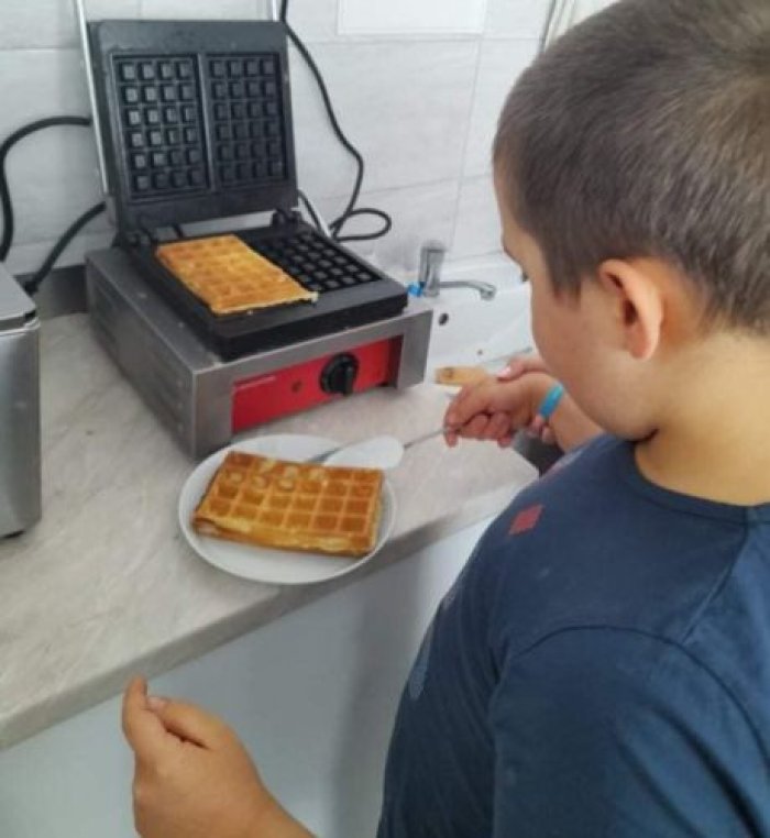 Uczeń za pomocą szpatułki wyciąga gofry z gofrownicy.