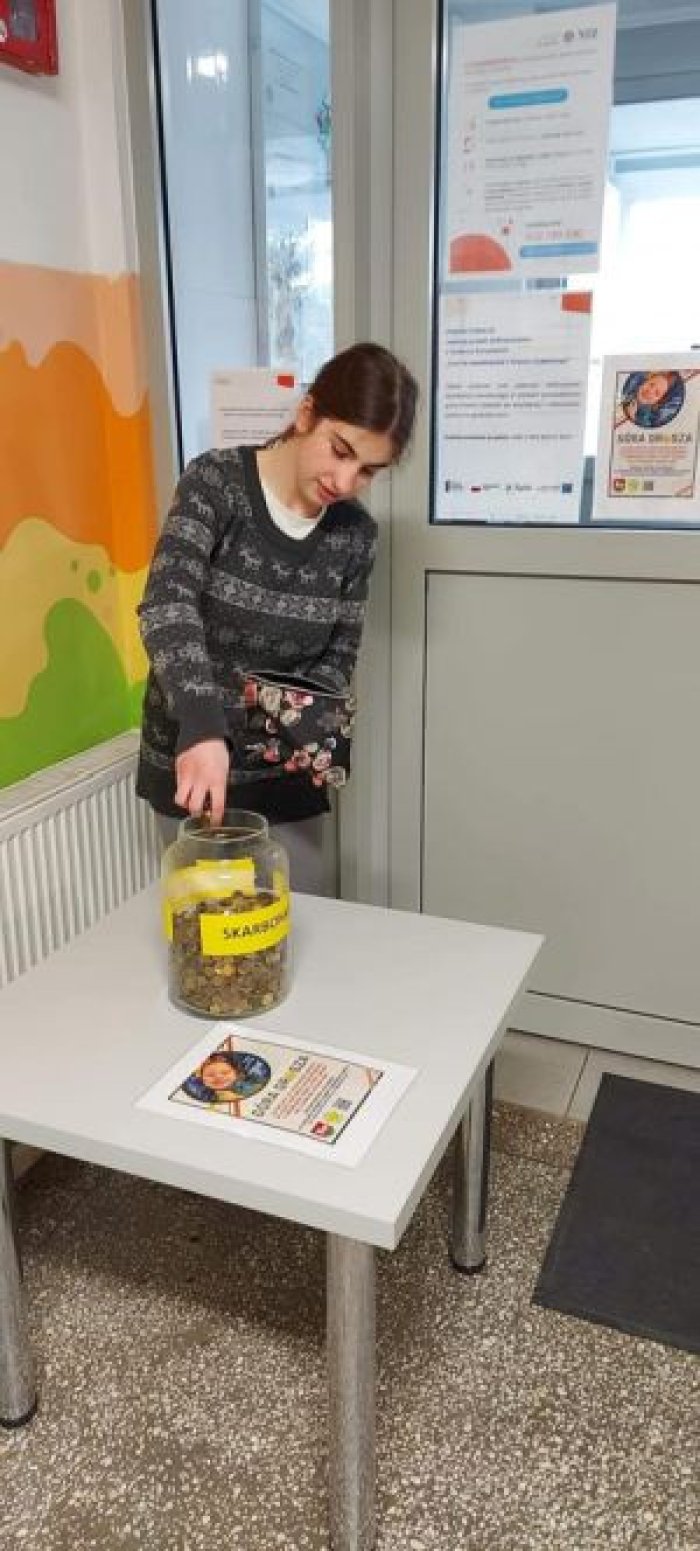 Uczennica wrzuca groszówki do skarbonki