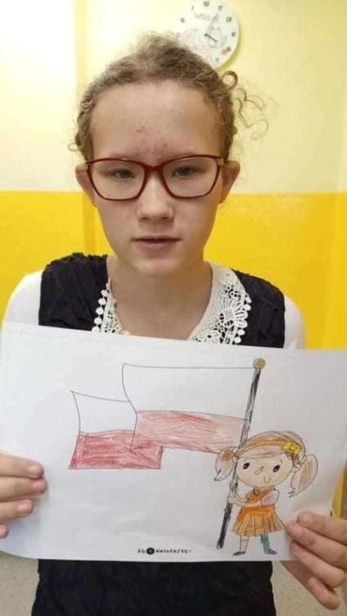 Uczennica prezentuje samodzielnie wykonaną przez siebie pracę plastyczną flagą Polski.