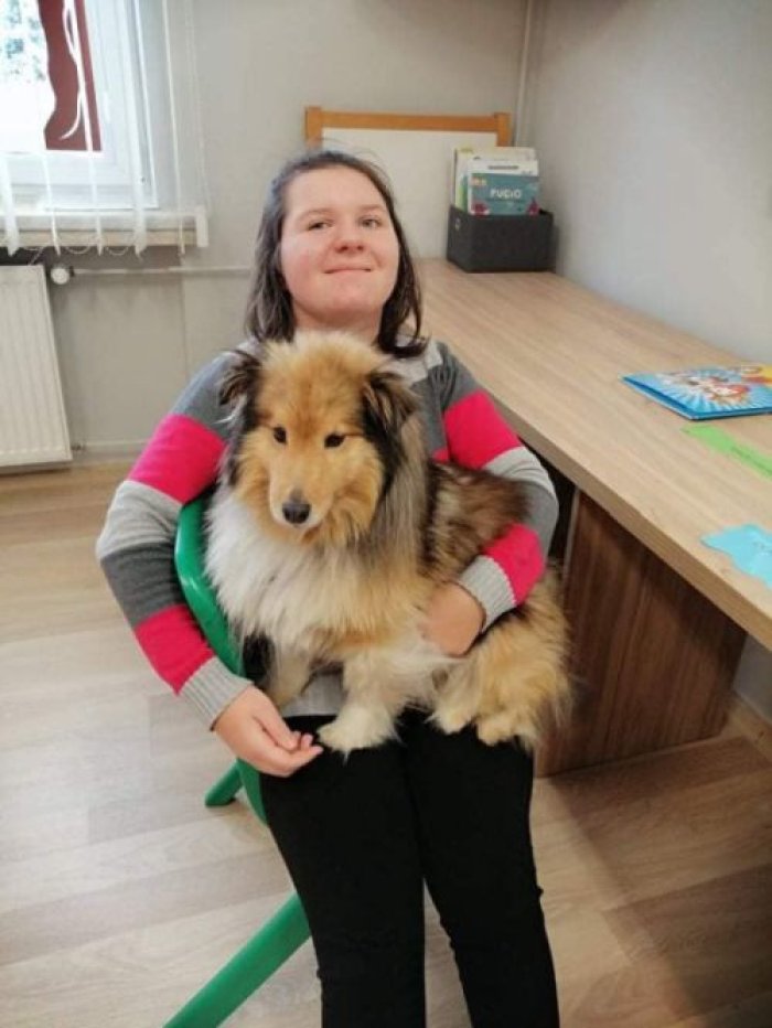 Uczennica trzyma psa terapeutycznego na kolanach.