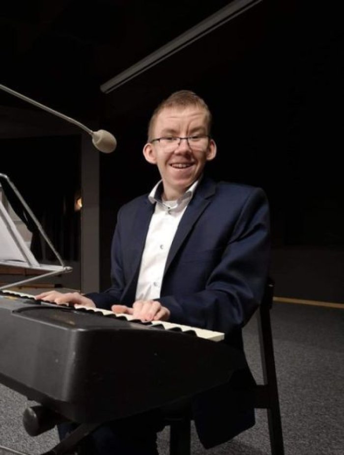 Laureat konkursu muzycznego Artur, pozuje do zdjęcia przy pianie.