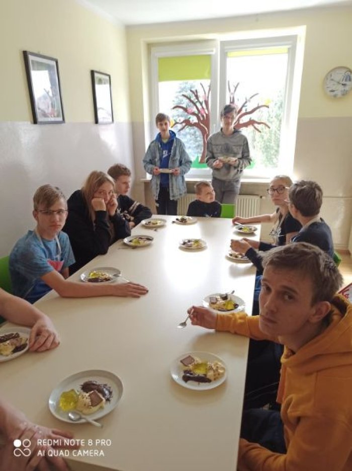 Wychowankowie internatu degustują [przy stole przygotowany deser.