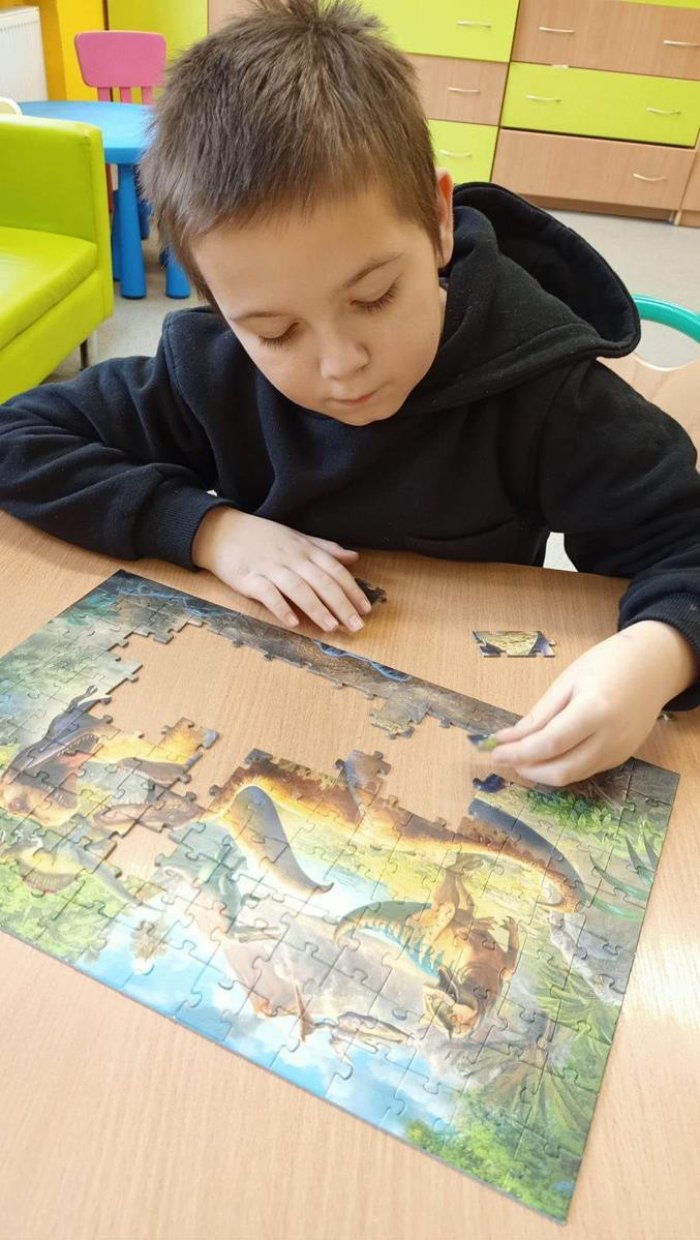Uczeń układa puzzle z dinozaurami.