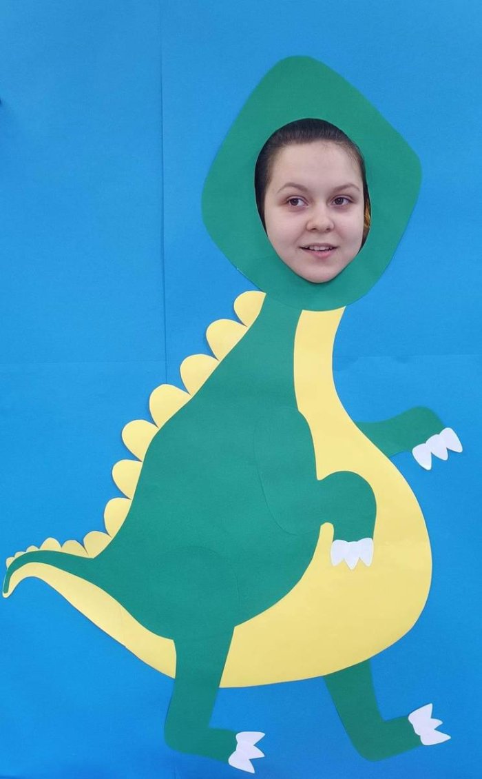 Uczennica w foto budce z dinozaurem.