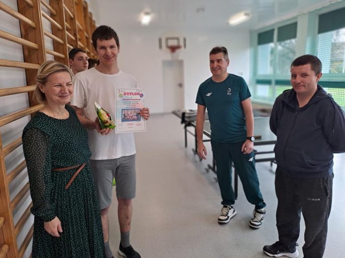 Uczestnik projektu pozuje do pamiątkowego zdjęcia z panią dyrektor szkoły i trenerami.