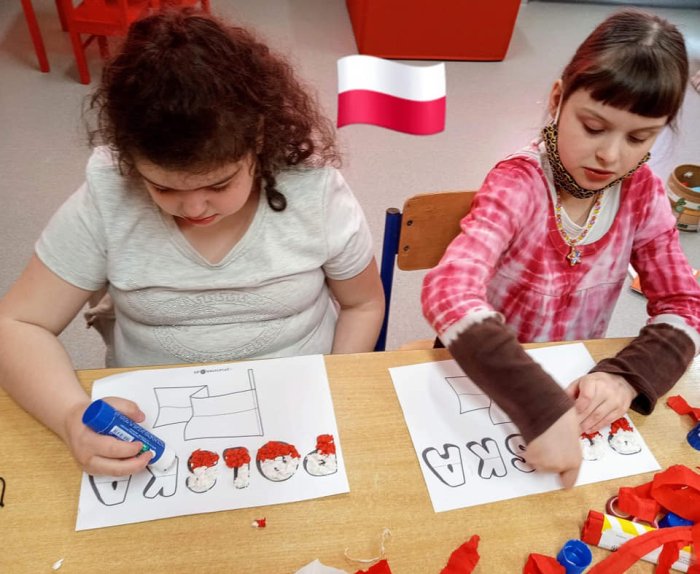Uczennice wyklejają za pomocą bibuły napis Polska. 