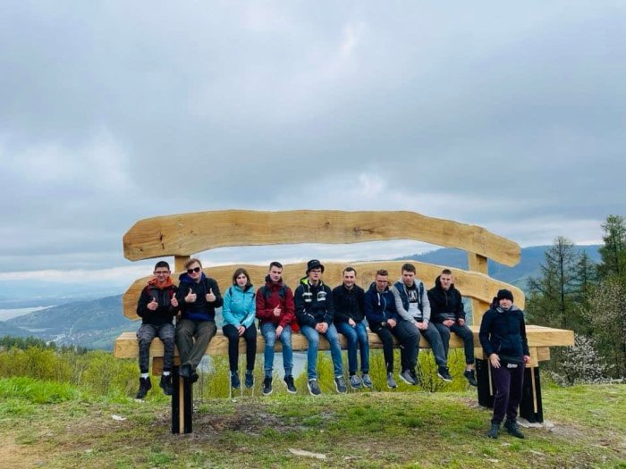 Uczniowie siedzą na wielkiej drewnianej ławce na tle panoramy Beskidów.
